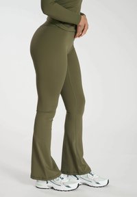 Olivgrön figurnära flare-byxor i stretchmaterial, med kontrastsömmar och sömlinsmidda midja, tillsammans med vita sneakers.