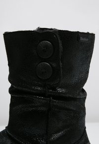 Czarne botki za kostkę wykonane z teksturowanego materiału, z dwiema dużymi czarnymi guzikami i małą metką Skechers z boku.