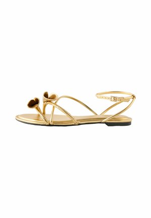 Goldene flache Sandale mit dünnen Riemen, Knöchelverschluss und zwei gedrehten blumenförmigen Akzenten am vorderen Riemen.