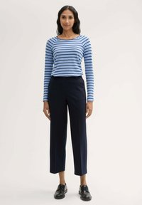 Langarmige blauw gestreepte top met een ronde hals, gecombineerd met marineblauwe wijde broek. Model draagt zwarte schoenen. Glad stoffen textuur.