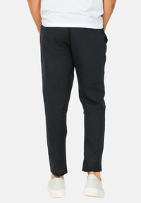 Pantaloni neri a sigaretta realizzati in tessuto leggero con una superficie liscia, dotati di tasche laterali e un design semplice. Indossati con sneaker bianche.