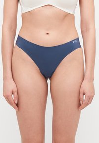 Mornarsko plava tangica izrađena od glatkog materijala s niskim strukom; sadrži logo Under Armour sa strane.