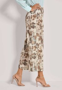 Bloemmotief wijde broek in crème met bruine en blauwe accenten, gemaakt van lichte stof, gecombineerd met naaktgekleurde strappy hoge hakken.