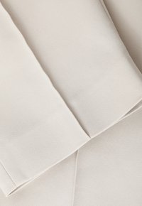 Béžová látka s hladkou texturou, s překládanými švy a záhybem, která vykazuje měkkou, neutrální barvu bez viditelných vzorů.