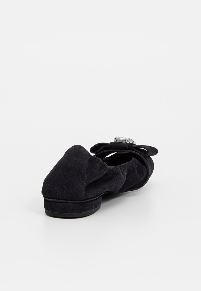 Schwarzer Wildlederschuh mit gerafften Seiten, einer dekorativen Schleife und einem großen rechteckigen Edelstein oben, von der Rückansicht gezeigt.