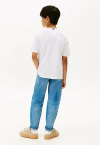T-shirt bianca a maniche corte con dettaglio a collo a V, abbinata a jeans in denim azzurro chiaro e sneakers beige. Design semplice e casual.