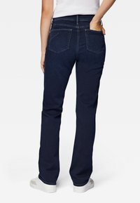 Jeans de mezclilla azul oscuro con diseño de pierna recta, bolsillos traseros y talle medio, combinados con zapatillas blancas.