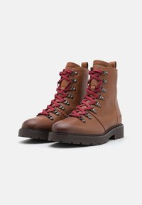 Botas de senderismo de cuero marrón con cordones rosas, ojetes metálicos, acabado texturizado y una suela negra y resistente para tracción.