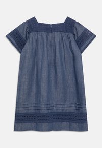 Jeansklänning med fyrkantig halsringning, korta ärmar och intrikata marinblå spetsdetaljer vid axlarna och fållen. Lätt textur, lös passform.