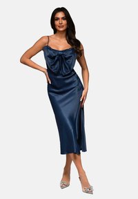 Navy satin midiklänning med en draperad rosettdetalj vid halsringningen, tunna axelband och en sidoklyfta, matchad med silverfärgade högklackade skor.