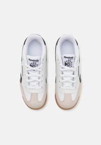 Reebok klassiske sneakers med et hvitt skinn overdel, svarte detaljer, grå semsket skinnpaneler og en såle i gummigummi, med flate hvite skolisser.
