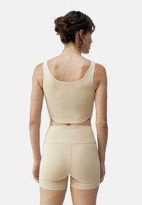 Beige sømløs sports-bh med tykke stropper, lav rygg og matchende høyt midje shorts. Glatt tekstur og fleksibelt stoff.