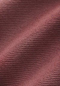 Gros plan sur un tissu tricoté bordeaux montrant la texture détaillée des mailles et des plis doux.