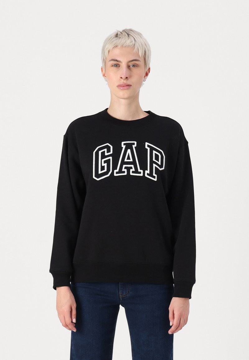 Juodas medvilnės džemperis su apvaliu kaklu, kuris turi baltą "GAP" logotipą per krūtinę. Ilgos rankovės ir gumbuoti rankogaliai.