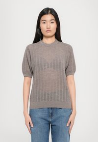 Pletený sveter s krátkymi rukávmi svetlohnedej farby s textúrovaným vzorom, s ribovaným výstrihom a lemom, skombinovaný s modrými džínsami.