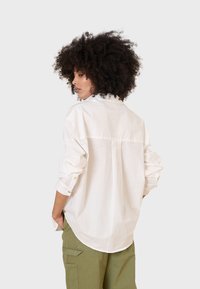 Camicia bianca a maniche lunghe con bottoni, dal fit morbido e maniche arrotolate, con yoke posteriore e una trama sottile, abbinata a pantaloni cargo verde oliva.