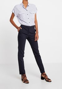 Niebiesko-biała koszula w paski z krótkim rękawem i dwoma przednimi kieszeniami, zestawiona z dopasowanymi czarnymi spodniami i czarnymi sandałami na paski.