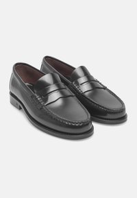 Black leather loafers with a smooth finish, featuring a stitched detail around the edge and a narrow strap across the top.