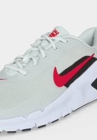 Λευκό παπούτσι για τρέξιμο Nike με κόκκινο λογότυπο Swoosh, λευκά κορδόνια και υφασμένο πλέγμα στο πάνω μέρος, εμφανιζόμενο από το πλάι και ελαφρώς από πάνω.