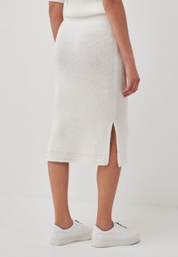 Witte gebreide midi-jurk met ribbeltextuur, een zijsplit en gestreepte zoomdetails. Gecombineerd met witte sneakers.