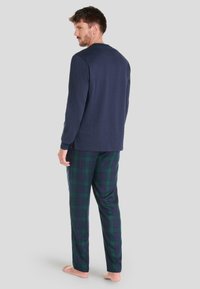 Camiseta de manga larga azul marino combinada con pantalones de pijama a cuadros verdes y azul marino. Tejido suave, corte relajado y escote tipo crew en la parte superior.