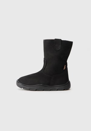 Botte d’hiver noire mi-mollet avec languette, tige en suède doux et semelle épaisse en caoutchouc pour une bonne accroche sur fond gris clair.