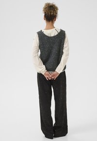 Szary wełniany kamizelka z okrągłym dekoltem, nałożona na białą bluzkę z długim rękawem z koronkowym wykończeniem, w zestawieniu z czarnymi spodniami w wzory.