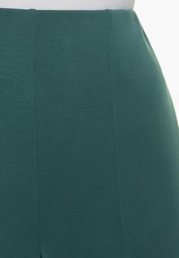 Tissu extensible teal, texture lisse, coupe ajustée, avec des coutures verticales et une taille haute, longueur mi-cuisse.