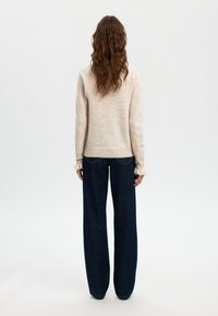 Maglione a maglia di un rosa chiaro, con maniche lunghe e polsini a coste, abbinato a jeans a gamba larga di un blu scuro, con leggera sfilacciatura all'orlo.