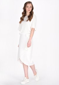 Witte, losse top met korte mouwen en elastische hem, gecombineerd met een witte wikkelrok met een zijstrik en een soepele textuur. Draag met witte sneakers.