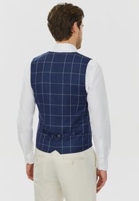 Granatowa kamizelka w kratkę z jasnoszarymi liniami, wykonana z tkaniny o splocie, z tylnym klapą i dwoma guzikami, w zestawie z białą koszulą.