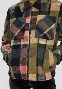 Polarowa kurtka w wielokolorowy wzór w kratę w odcieniach zieleni, różu i czerni, z zamkiem z przodu i dwiema kieszeniami na piersi.