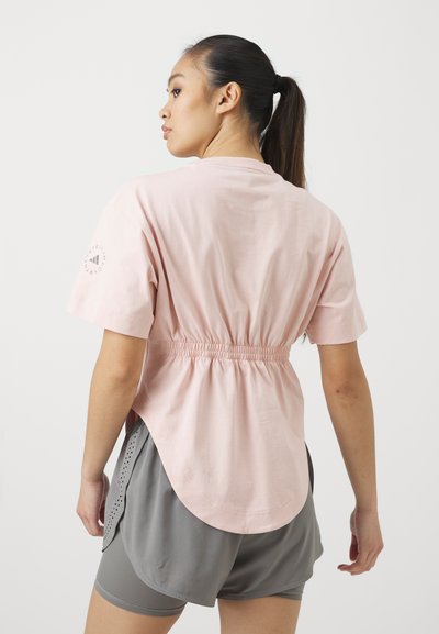 Kortermet rosa T-skjorte med elastisk midje, buet nederkant og dekorativ logo på armen. Kombinert med grå shorts med perforerte sider.
