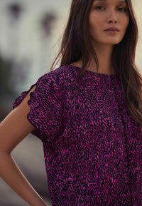 T-shirt à manches courtes en imprimé léopard rose et noir, avec un col rond et un tissu texturé avec des détails froncés sur les manches.