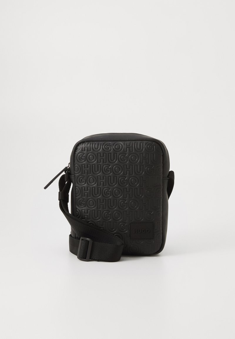 Crni pravokutni crossbody ranac s reljefnim ponavljajućim tekstom "HUGO" i podesivim crnim remenom na bijeloj pozadini.
