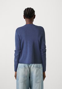 Dunkelblaues Langarm-Sweatshirt mit rundem Ausschnitt, aus einem glatten Stoff gefertigt. Getragen mit hellblauen lässigen Jeans.