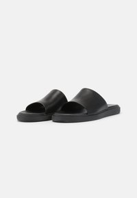 Crne slip-on sandale od glatke kože, s otvorenom prstima, minimalističkim dizajnom i debelim đonom za udobnost.