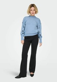 Světlé modrý pletený svetr s květinovou výšivkou na rukávech, spárovaný s černými zvonovými kalhotami a černými špičatými balerínami.