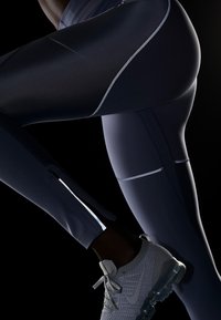Námořnické sportovní legíny s reflexními švy a zipovými otvory, kombinované se šedými teniskami s texturovaným designem a průhlednými podrážkami.