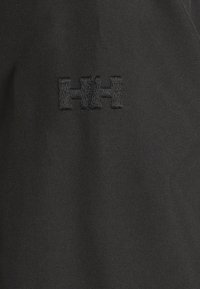 Tessuto nero con una superficie texturizzata e un logo ricamato in filo scuro, che enfatizza un design minimalista.