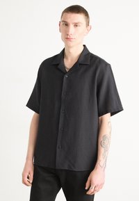 Camisa de botones negra de manga corta hecha de tela texturizada, con cuello y botones negros, combinada con pantalones negros.