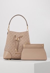 Sac seau beige Michael Kors avec un motif monogramme et des accessoires dorés, associé à une pochette zippée beige uni sur une surface blanche.