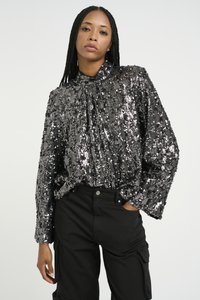 Svart glitrende topp med plisseringsdesign, høy hals og lange ermer. Kombinert med svarte cargo bukser.