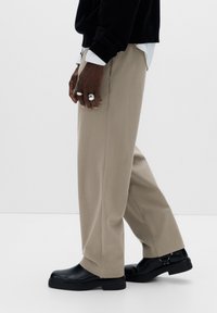 Beige széles szárú nadrág sima anyagból, fekete bőr csizmával párosítva. Jellemzői a szabott fazon és a minimalista dizájn.