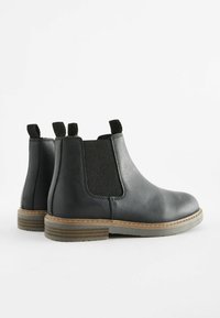 Svarta läder Chelsea-boots med elastiska sidopaneler, en texturerad yta, dragflikar och kontrasterande brun sula. Rund tådesign.