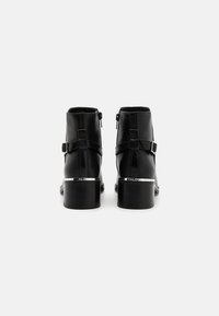 Bottines en cuir noir avec deux zips latéraux, des sangles décoratives et un accent argenté au talon. Texture lisse et design à bout rond.