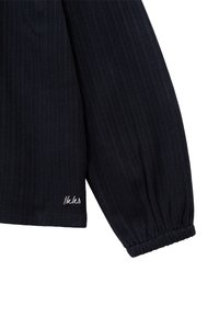 Granatowa, prążkowana bluzka z długim rękawem i elastycznymi mankietami, z małym białym haftowanym logo w pobliżu dołu, na białym tle.