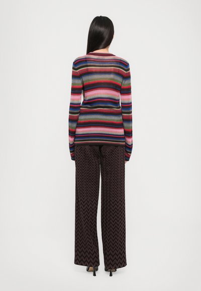 Multifarvet stribet sweater med lange ærmer, parret med bredbenede bukser med zigzag-mønster i mørke nuancer, der skaber en lagdelt tekstur.