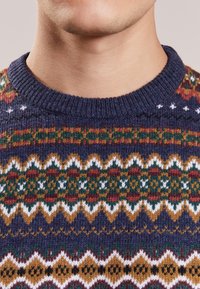Kötött pulóver kerek nyakkal, tarka Fair Isle mintával, tengerészkék, piros, zöld, arany és fehér árnyalatokban. Puha tapintású.