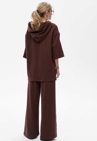 Brązowa, oversize'owa bluza z kapturem, z krótkimi rękawami oraz dopasowanymi spodniami o szerokich nogawkach, wykonana z miękkiego materiału. Charakteryzuje się luźnym krojem i minimalnym zdobieniem.